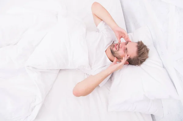 Dolores de cabeza por migraña. Hombre guapo relajándose en la cama. Los ronquidos pueden aumentar los dolores de cabeza de riesgo. Síntoma común de apnea del sueño. Causas de dolor de cabeza temprano en la mañana. Los problemas para dormir pueden provocar dolores de cabeza por la mañana. —  Fotos de Stock