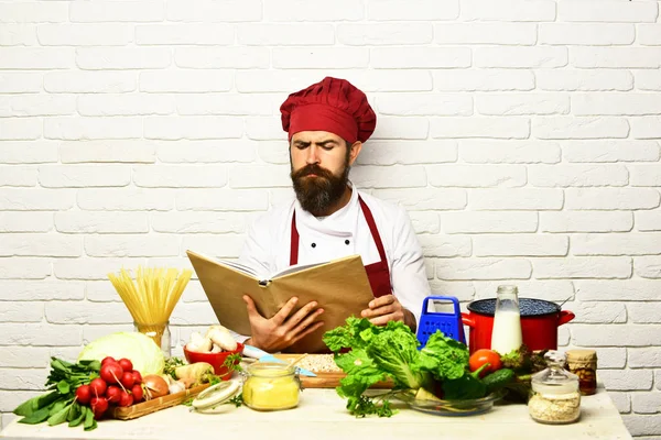 Cozinhe com cara séria em uniforme senta-se por verduras — Fotografia de Stock
