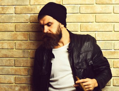 Beyaz sakallı, beyaz tenli hippi bej tuğlalı stüdyo arka planında puro içiyor.