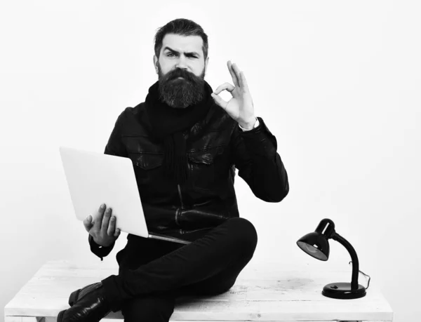 Bearded brutal caucasian hipster sitting on table with laptop — Stock Photo, Image