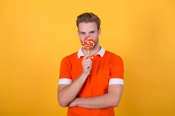 Feliz comiendo dulces. Símbolo de felicidad. Dulce chico. Sabor a infancia. El hombre come piruleta. Hombre sonriente espera piruleta. Concepto de vacaciones. Azúcar perjudicial para la salud. Chico piruleta caramelo amarillo fondo — Foto de Stock