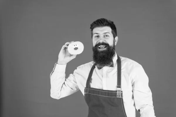 Cozinhamos para ti. Cozinheiro confiante. Cozinheiro profissional segurando donut no fundo vermelho. Homem barbudo vestindo avental de cozinheiro — Fotografia de Stock