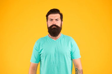 ciddi sakallı adam sarı arka plan, erkek yaz modası. Acımasız ve kendinden emin. Olgun berber dükkanı müdürü. Sakallı, olgun bir hippi. Bıyıklı, vahşi, beyaz bir hippi. Erkek berber bakımı