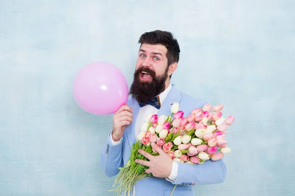 Geschenkstrauß vorhanden. Geschenk für den Ehepartner. Mann mit Luftballon. Geburtstagsfeier. Bartträger Hipster mit Blumenstrauß. 8. März. Blumen für den Frauentag. Bärtiger Mann mit Tulpen. Frühlingsstimmung. Liebesdatum — Stockfoto