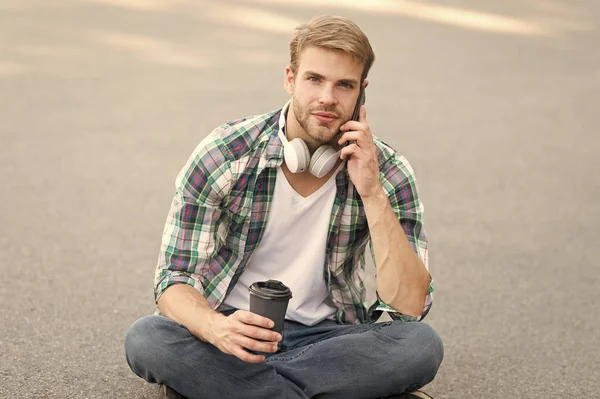 important call. phone call. listen music. ebook concept. man checkered shirt. student relax and recharge. coffee to go. guy drink coffee outdoor. man sit on ground. carefree student in headset