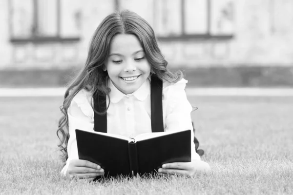 Extrakurrikulär avläsning. Söt liten barnbok utomhus. En söt liten flicka lär sig läsa. Skolflickans skoluniform ligger på gräsmattan med favoritbok. Studerar koncept. Grundutbildning — Stockfoto