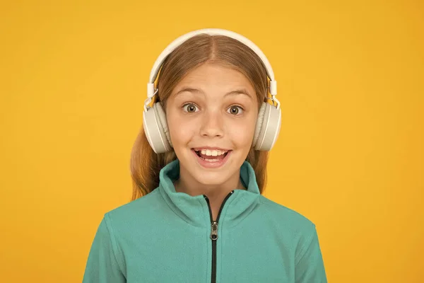 A canção feliz faz-lhe sorrir. Menina pequena feliz ouvir música no fundo amarelo. Criança gosta de cantar em fones de ouvido. Sorri na cara feliz. A música tem emoções felizes — Fotografia de Stock