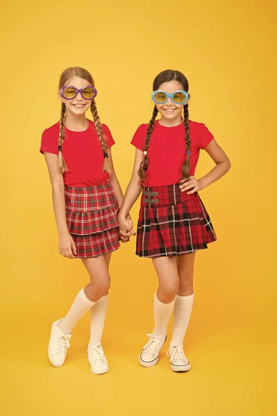 Um acessório de verão. Meninas irmãs bonitos roupas semelhantes usam óculos de sol coloridos para a temporada de verão. Tendência de moda verão. Crianças amigos da moda posando em óculos de sol no fundo amarelo. Diversão de verão — Fotografia de Stock