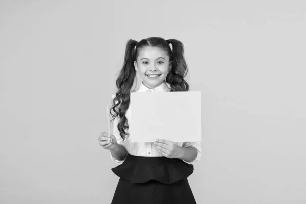 Prends un stylo. Petite fille tenant feuille de papier vierge pour la tâche d'écriture sur fond jaune. Petit enfant affiche affiche verte pour l'écriture d'informations. Carte d'exposition vide pour l'écriture, espace de copie — Photo