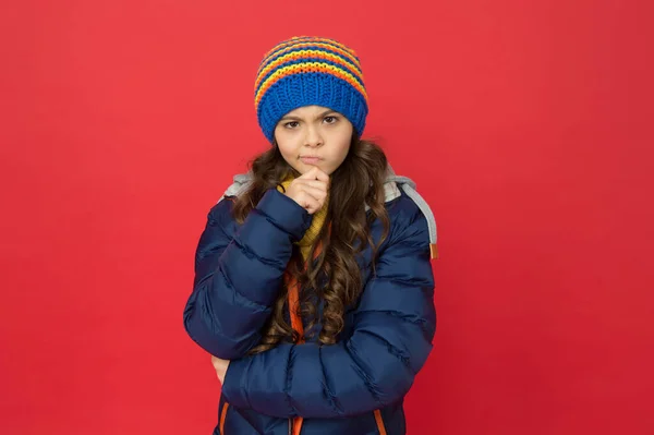 Relutante em fazer alguma coisa. Miúdo cauteloso e duvidoso. Menina usar roupas de inverno fundo vermelho. Conceito de infância. Menina emocional chapéu de malha de cabelo longo. Adolescente estilo casual menina. Emoções e humor — Fotografia de Stock