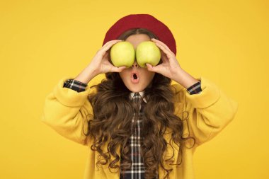 Hasadı etkiledi. Şirin, uzun kıvırcık saçlı bir kız elma tutuyor. Çocuk kız duygusal yüz ifadesi. Lezzetli hasat. Hasat mevsimi. Çocuk elinde elma tutarken şaşırdı. Sağlıklı gıda konsepti