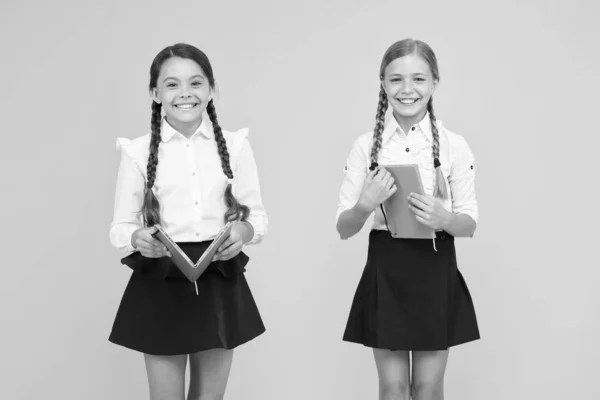 Schoolgirls study together on yellow background. Study language. Cute children study with textbook. Practice and improve reading skills for school studies. Back to school concept. Girls hold book