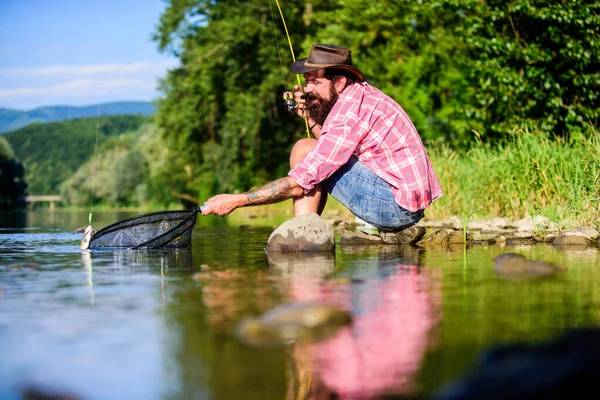 Pescador exitoso en el agua del lago. pesca de caza mayor. relajarse en la naturaleza. pesca hipster con cuchara-cebo. hombre barbudo maduro con pescado en caña. pasatiempo peces mosca. Actividad de verano. Qué pez. —  Fotos de Stock