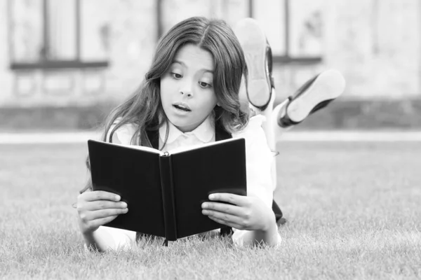 学习概念。课外阅读。可爱的小孩在户外看书.基础教育。可爱的小女孩学习阅读。女校校服躺在草坪上，上面有一本心爱的书 — 图库照片