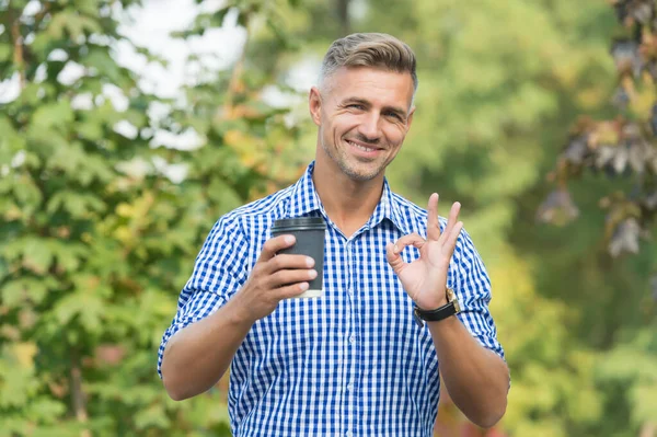 Capuchino perfecto. Propietario de plantación de café. Hombre bebiendo taza de papel de café. Un sorbo más. Beber café en el camino. Relájate y recarga. Guapo sonriente chico hold taza naturaleza fondo soleado día — Foto de Stock