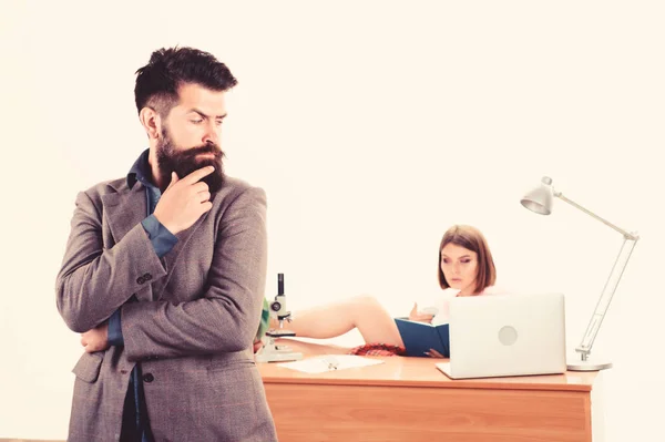 Looking like big boss man. Bearded man looking at sexy woman working in background. Confident business man and secretary in office. Brutal caucasian man with long beard in business wear