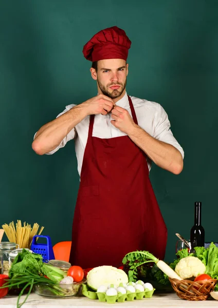 Chef with serious face adjusts collar on dark green background. — Stock Photo, Image