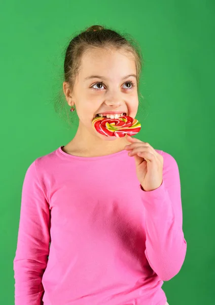 Kind met hongerig gezicht poseert met snoep op groene achtergrond. — Stockfoto