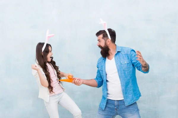 funny competition. father and daughter start carrot fight. have fun in hare costume. dad and child wear bunny ears. Spring mood. easter family party. happy easter concept. carrot for my little rabbit