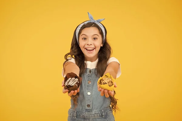 Concepto de panadería y confitería. Niña sostiene magdalenas acristaladas. Deliciosos pastelitos. Feliz infancia. Adorable niño sonriente con cupcakes sobre fondo amarillo. Café restaurante de comida. Deliciosas magdalenas —  Fotos de Stock