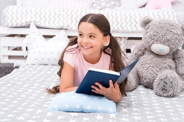 Once upon a time. Girl child in bed read book with teddy bear plush toy. Pleasant time in cozy bedroom. Girl kid long hair cute pajamas relax and read book. Book about love. Favorite fairy tale
