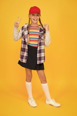 At kuyruklu hippi. Küçük mutlu hipster beyzbol şapkası sarı arka plan giyer. Havalı görünüşlü sevimli hippi gülüşü. Hippi tarzında sevimli bir çocuk.