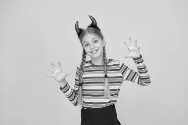 O şeytan. Cadılar Bayramı partisi kızı sarı arka plan. Küçük kız kırmızı şeytan boynuzu takıyor. Cadılar Bayramı görünüşlü gizemli kız. Küçük kız kötü bir şeytana dönüştü.