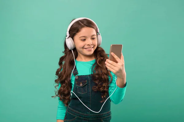 Zwykła moda dla dzieci. Dzieciak długie włosy słuchać muzyki w słuchawkach. małe dziecko zrobić listę odtwarzania na smartfonie. Mała dziewczynka używa odtwarzacza mp3. studiować we współczesnym życiu. uczennica korzystać z urządzenia cyfrowego — Zdjęcie stockowe