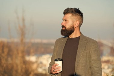 Kafein bağımlısı. Hippi bardağı kafein enerji içeceğiyle birlikte tutar. Sakallı adam açık havada sıcak kafeinli içecekle şarj oluyor. Sabah kafeinle daha iyi olur.