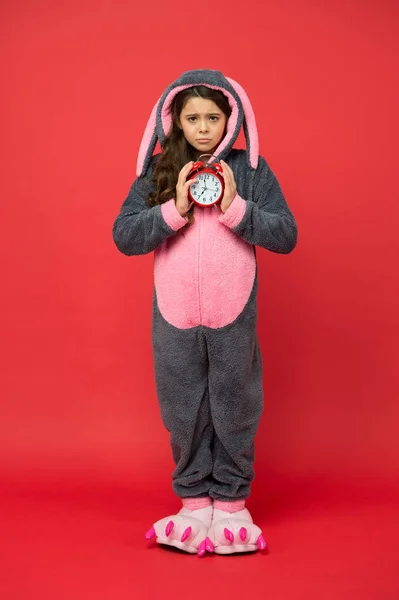 Alarme du matin. La journée commence normalement. Adorable réveil lapin. Petite fille en costume de lapin. Enfant lapin kigurumi. Pyjama lapin fille. Bunny kid fond rouge. Petit animal. Temps de comptage — Photo