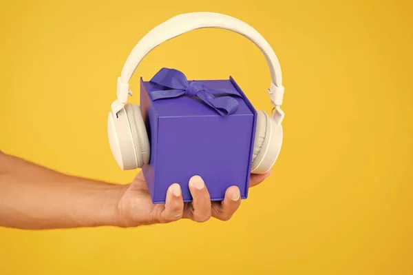 music gift conept. gift box with headphones. male hand hold present yellow backdrop. modern headset. what is inside. audio accessories sale. christmas music gift. musical present. convenient delivery