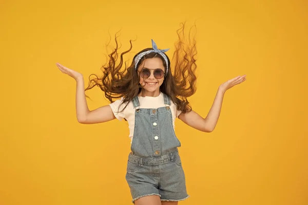 Je kapsel de hele dag laten meegaan. Gelukkig kind met krullend kapsel vliegen op gele achtergrond. Klein schattig meisje glimlachend met lange golvende kapsel. Fashion look van kapsel met glamoureuze krullen — Stockfoto