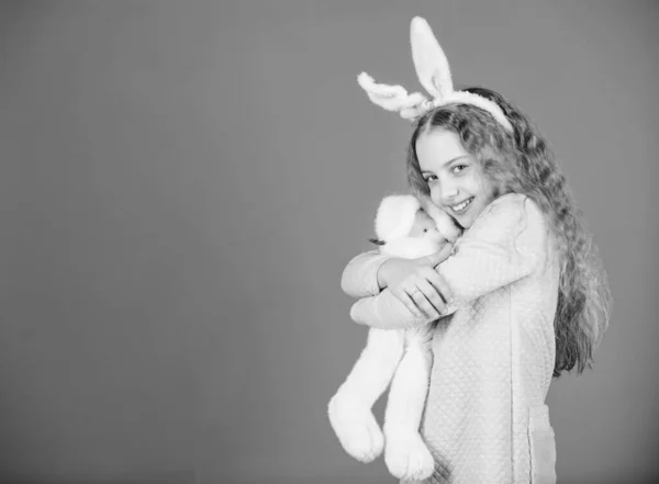 Conejita con lindo juguete sobre fondo azul. Niño sonriendo jugar conejito juguete. Feliz infancia. Adéntrate en el espíritu de Pascua. Accesorio de orejas de conejo. Precioso niño conejito juguetón con el pelo largo. Lindo y adorable — Foto de Stock