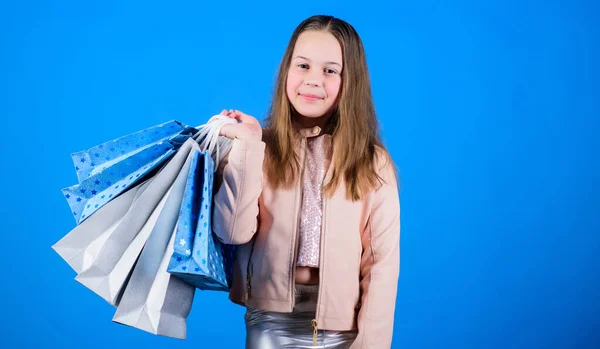 Ahorros en compras. Niños felices. Niña compras en línea sobre fondo azul. Ventas y descuentos. Moda infantil. asistente de tienda con paquete. Niña pequeña con bolsas de compras. espacio de copia —  Fotos de Stock