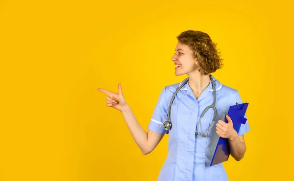 Indossa uno stetoscopio. infermiera che tiene il legante e indossa lo stetoscopio. Dottoressa sorridente con una cartella in uniforme in piedi. Ritratto di bella infermiera con una cartella. copia spazio — Foto Stock