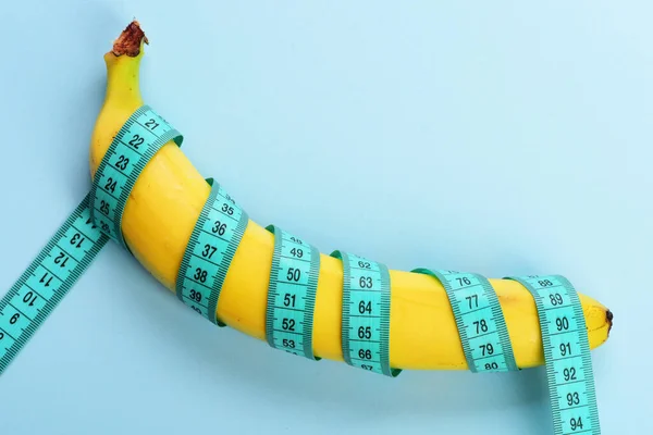 Righello centimetro ruotato intorno alla frutta fresca. Banana con nastro blu per la misurazione della figura — Foto Stock