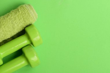 Parlak yeşil renkli dambıllar ve yeşil arka planda havlu.