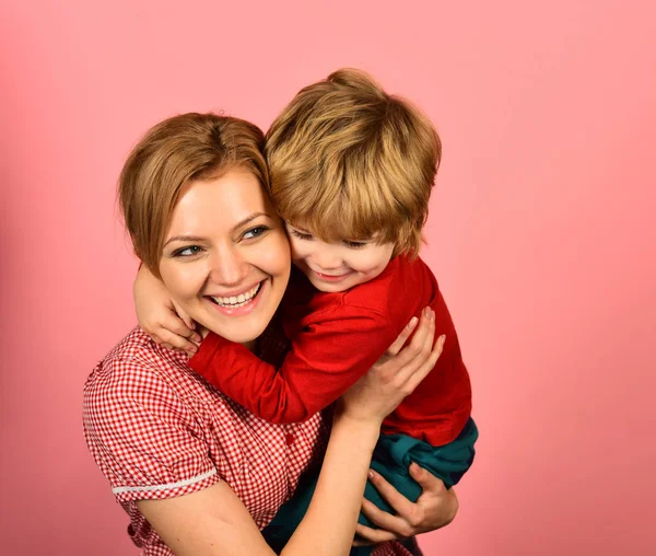 Mother hugs son on pink background. Woman and little boy