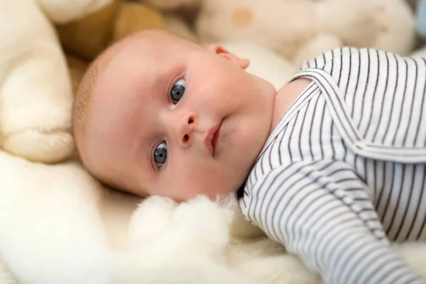 ストライプのボディスーツの赤ちゃん。赤ん坊は白い子牛に横たわっ. — ストック写真