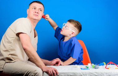 Küçük doktor, masada tıbbi aletlerle oturuyor. Hastalık tedavisi. Baba ve oğul tıp hanedanlığı. Tıbbi muayene. Tatlı çocuk ve babası doktor. Hastane çalışanı. Sağlık hizmetleri. Tıp konsepti