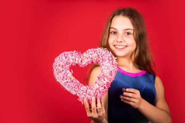 Creas mi sonrisa de corazón. Niño feliz con el corazón rojo de fondo. Niña con corazón de mimbre rosa. Decoración en forma de corazón para el día de San Valentín. Vacaciones de amor y cuidado, espacio de copia — Foto de Stock