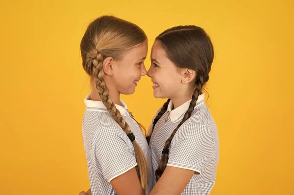 Vriendelijke knuffel. Leuke schoolmeisjes. Meisjes gevlochten kapsel. Vrolijke schoolmeisjes gele achtergrond. Kleine meisjes spelen met leuke vlechten. Mooie schoolmeisjes beste vrienden. Terug naar schoolconcept — Stockfoto