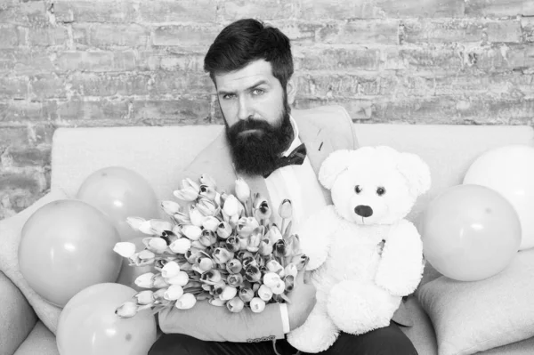 Avec quel succès lui demander sortir ensemble. Homme romantique avec des fleurs et un ours en peluche assis sur le canapé attendant petite amie. Cadeau romantique. Macho rendez-vous romantique prêt. Homme porter bleu tuxedo nœud papillon tenir bouquet de fleurs — Photo
