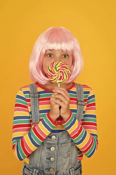 Dulce diente. Niño pequeño sostiene caramelo lollipop fondo amarillo. Niña con arcoíris remolino caramelo en palo. Niño adorable disfrutar de postre de caramelo de azúcar. La mejor tienda de dulces — Foto de Stock