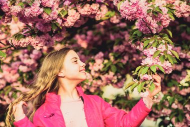 Bahar zamanı cilt için doğal kozmetik ürünleri. Bahar çiçeğindeki küçük kız çocuğu çiçek açar. Kiraz çiçekli mutlu kız. Sakura ağacı çiçek açıyor. Çiçek kokusu, alerji. Yaz. Çocukluk güzelliği