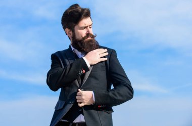 Erkek sakalı ve bıyığı resmi kıyafetler giyer. Çok doğru. İş adamı sakallı, gökyüzü geçmişi olan. Kusursuz kıyafet. Erkek takım elbisesi ceketi ayarlıyor. Erkek moda erkek giyimi. Moda eğilimi