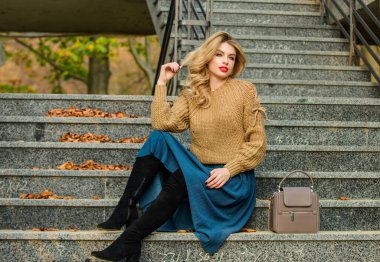 Kız eteğinin üstüne daha büyük bir katman örülmüş. Sonbahar formülü. Sonbahar için Süveter ve Etek Kombo stili. Harika saç stili olan kadın merdivenlerde dışarıda oturuyor. Sonbahar moda trendi. Giyilebilir trendler