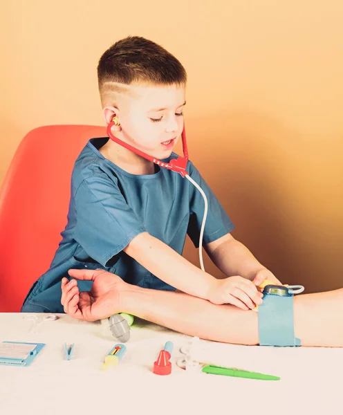 Examen médico. Educación médica. Niño lindo niño futuro médico carrera. Salud. El niño pequeño médico se sienta en la mesa con estetoscopio y herramientas médicas. Concepto de medicina. Medición de la presión arterial — Foto de Stock