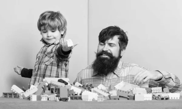 Otec hraje hru. Otec a syn vytvářejí barevné stavby s cihlami. Rozvoj dětské péče a výchova. Vousatý otec a chlapec hrají spolu. Otec a dítě postavili plastové bloky — Stock fotografie