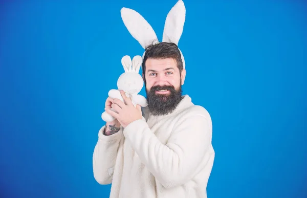 Meant for hugging. Happy hipster with long rabbit ears holding bunny toy. Fertility and new life. Bearded man in easter rabbit costume with hare toy. Easter rabbit is a spring symbol of Easter